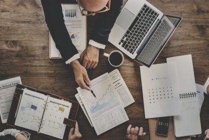 Homem de negócios observando relatórios em cima de uma mesa com computador e papéis, observando os índices do MTBF.