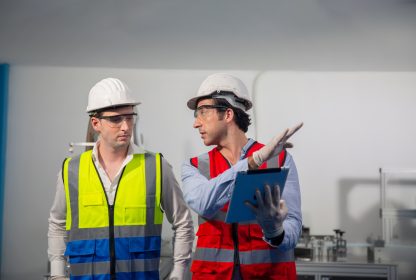 Checklist online: trabalhadores com equipamentos de segurança analisam máquina em um laboratório e fazem anotações.