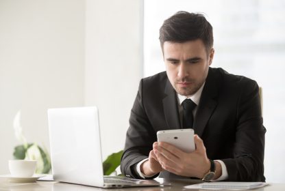 Monitoramento remoto: homem com expressão séria olha para tela do celular em um escritório.